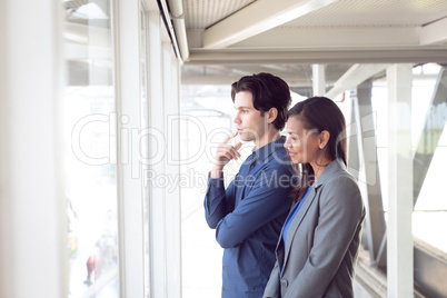 Male and female architects looking through window in office