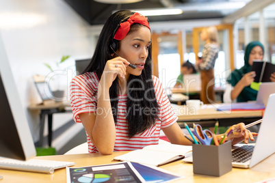 Female customer service executive talking on headset and working on laptop in a modern office