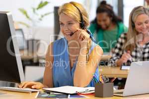 Female customer service executive talking on headset and working on computer in a modern office