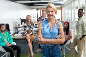 Businesswoman with arms crossed looking at camera while diverse colleagues standing in background