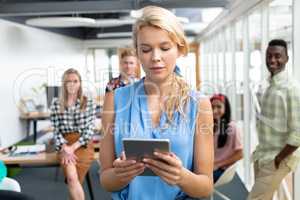 Businesswoman using digital tablet while diverse colleagues standing in background at office