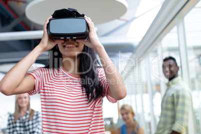 Businesswoman using virtual realty headset while diverse colleagues standing in background