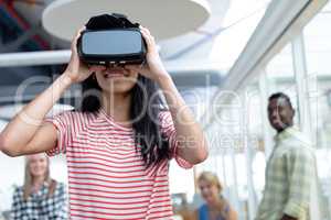 Businesswoman using virtual realty headset while diverse colleagues standing in background