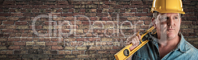 Male Contractor In Hard Hat Holding Level In Front Of Brick Wall