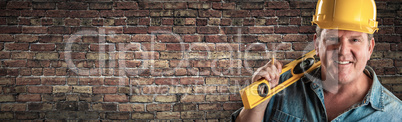 Male Contractor In Hard Hat Holding Level In Front Of Brick Wall