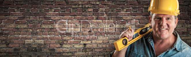 Male Contractor In Hard Hat Holding Level In Front Of Brick Wall