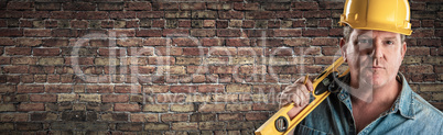 Male Contractor In Hard Hat Holding Level In Front Of Brick Wall