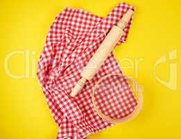 wooden rolling pin on a red textile napkin and a round sieve