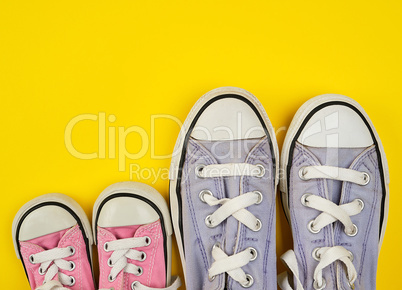 two pairs of worn textile shoes of different sizes on a yellow b