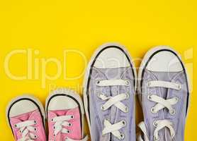 two pairs of worn textile shoes of different sizes on a yellow b