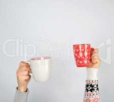two hands in a sweater holding  ceramic mugs on a white backgrou