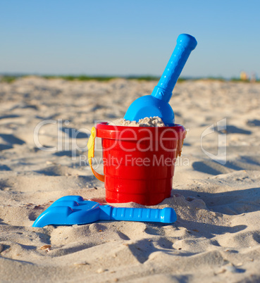 red plastic bucket and blue rake, shovel on the sand