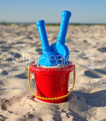 red plastic bucket and blue rake, shovel on the sand