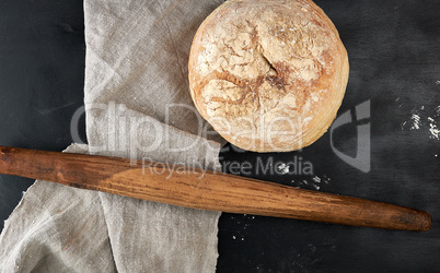 round baked bread and wooden old rolling pin on a black table