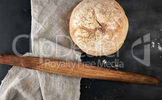 round baked bread and wooden old rolling pin on a black table