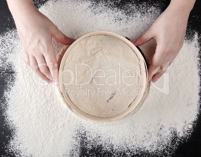 women's hands hold a round wooden sieve and sift white wheat flo