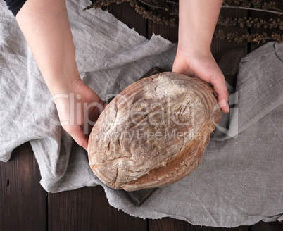 women's hands hold a whole round loaf of rye flour bread