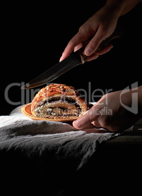 female hands cut baked roll with poppy seeds on a wooden plate