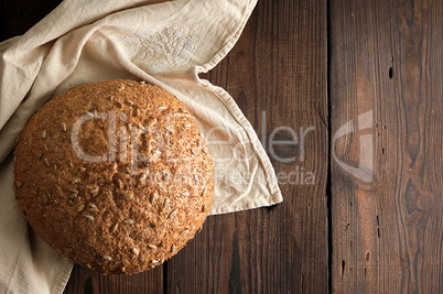 baked round rye bread with sunflower seeds on a beige textile na