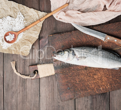 fresh whole sea bass fish and knife on brown cutting board