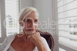 Active senior woman with hand on chin sitting on chair in a comfortable home