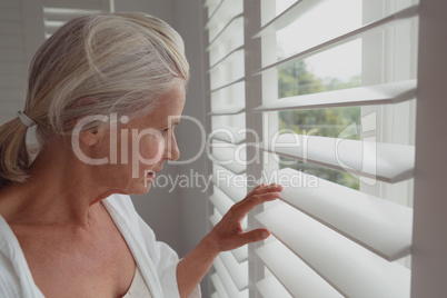 Active senior woman looking through window in a comfortable home