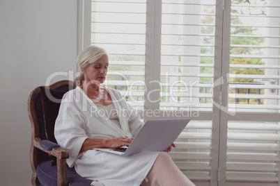 Active senior woman using laptop on chair in a comfortable home