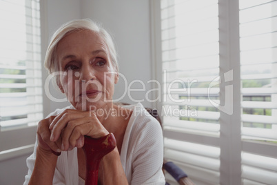 Active senior woman leaning on walking cane and looking away in a comfortable home