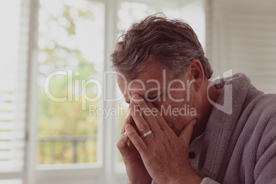 Sad active senior man with hands on face in a comfortable home