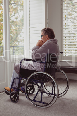 Disabled active senior man looking through window on wheelchair in a comfortable home