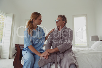 Female doctor consoling active senior man on bed in bedroom at comfortable home