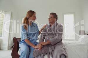 Female doctor consoling active senior man on bed in bedroom at comfortable home