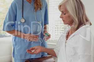 Female doctor giving medicine to active senior woman in bedroom at home