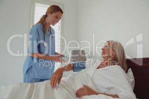 Female doctor checking blood pressure of active senior woman in bed in bedroom