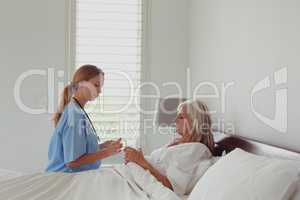 Female doctor giving medicine to active senior woman in bedroom
