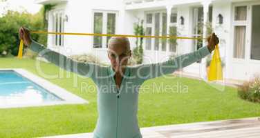 Active senior woman exercising with resistance band in porch at home