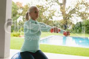 Active senior woman exercising with dumbbell in porch at home