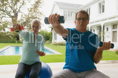 Active senior couple exercising with dumbbell in porch at home