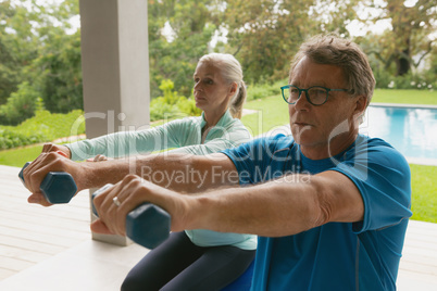 Active senior couple exercising with dumbbell in porch at home