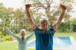 Active senior couple exercising with resistance band in porch at home