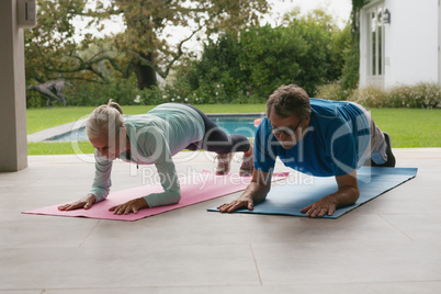 Active senior couple doing plank exercise in the porch at home