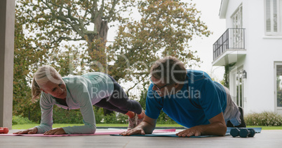 Active senior couple doing plank exercise in the porch at home