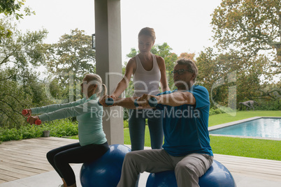 Female trainer assisting active senior couple to exercise with dumbbell in the porch