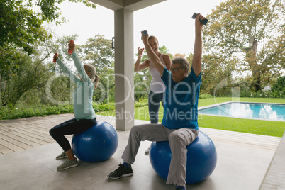Female trainer assisting active senior couple to exercise with dumbbell in the porch