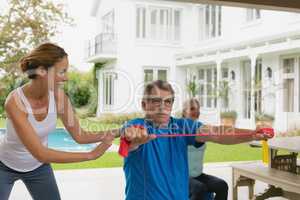 Female trainer assisting active senior couple to exercise with resistance band in the porch