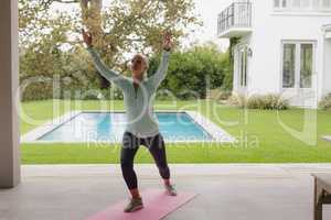 Active senior woman doing yoga on exercise mat in the porch at home