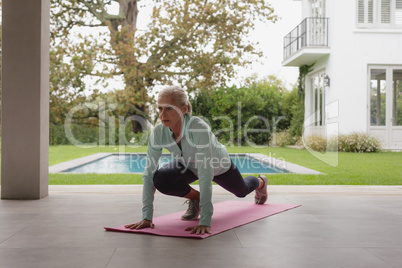 Active senior woman doing yoga on exercise mat in the porch at home