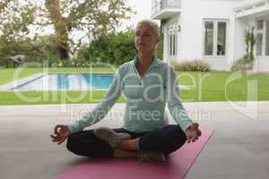 Active senior woman doing yoga on exercise mat in the porch at home