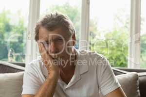 Active senior man with hand on face sitting on sofa in a comfortable home
