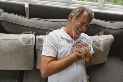 Active senior man suffering from chest pain on sofa in a comfortable home